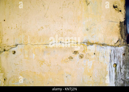 Yellow plastered wall with visible deterioration and cracks form an old building in need of restoration.