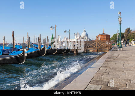 Gondolas with wave splash on an Acqua Alta high  tide, San Marco, Venice, Italy looking along the row of ferros or metal ornaments on the prow Stock Photo