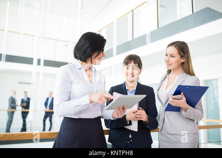 Mature female professional discussing over tablet computer with colleagues in office Stock Photo