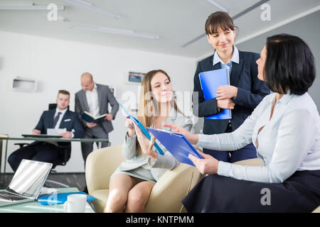 Female executives discussing over clipboards with male colleagues in background at office Stock Photo