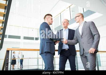 Low angle view of businessmen shaking hands while standing by railing in office Stock Photo