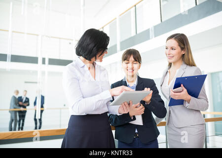 Mature female professional discussing over tablet computer with smiling colleagues in office Stock Photo