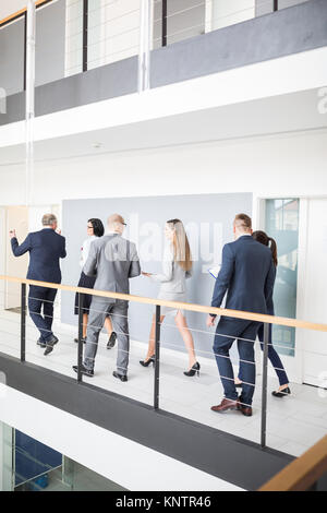 Full length of business colleagues discussing while walking on corridor by railing in office Stock Photo