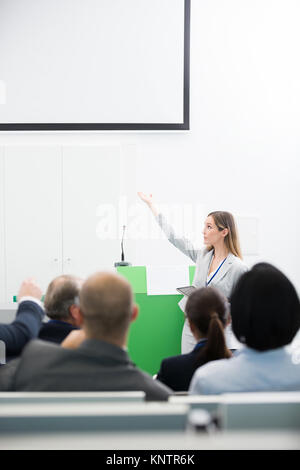 Female professional giving presentation to audience in lecture hall Stock Photo