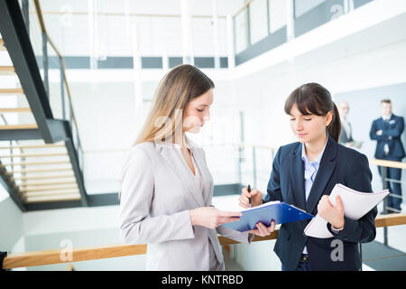 Female business colleagues discussing over documents by railing in office Stock Photo