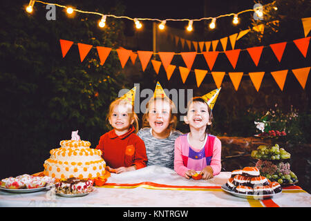 Children's birthday party. Three cheerful children girls eating cake with their hands and smearing their face. Fun and festive mood in the decorated c Stock Photo