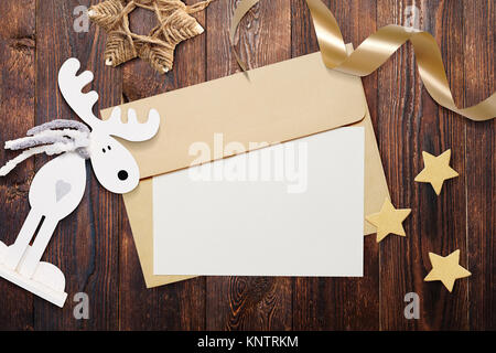 Christmas mockup envelope with blank paper on brown wooden background. Letter to Santa Claus. Christmas winter setting - star, elk, ribbon Stock Photo