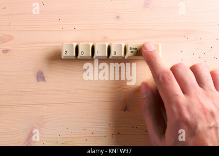 Index finger presses on the keyboard, on which is written 2018 and enter ket on a wooden background. New year 2018 card. Stock Photo