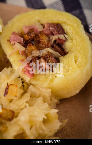 Vertical photo with vintage plate with portion of potato dumplings filled by smoked pork meat together with sour cabbage and fried onion. Checkered bl Stock Photo