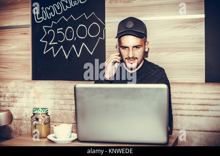 Young man talking on the phone, using laptop computer and drinking coffee in a coffee shop Stock Photo