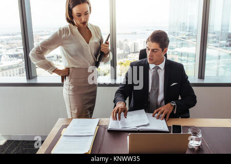 Two business people discussing contract documents together in office. business executives going through papers in office. Stock Photo