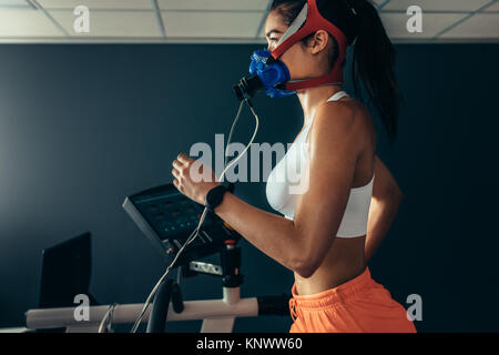Side view of professional sportswoman with mask running on treadmill in gym. Female athlete in sports science lab measuring her performance and oxygen Stock Photo