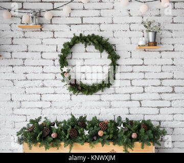Closeup view of round elegant Christmas wreath hanging on white brick wall. Wreath decorated with ratten balls, dried flowers of lotus and wooden star Stock Photo