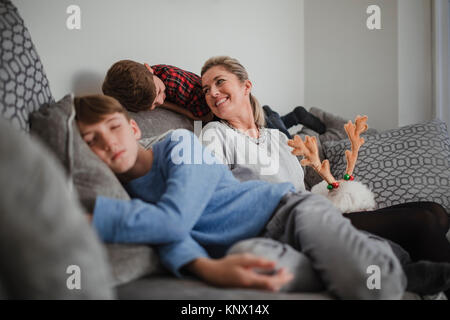 Mother is relaxing with her two sons and her pet dog on the sofa at home. Stock Photo