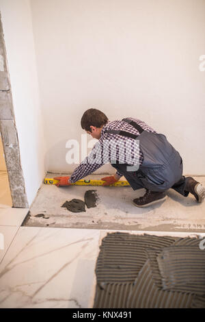 Home tile improvement - handyman with level laying down tile floor Stock Photo