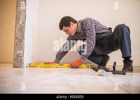 Home tile improvement - handyman with level laying down tile floor Stock Photo