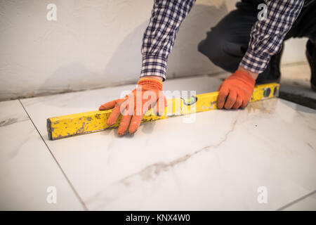 Home tile improvement - handyman with level laying down tile floor Stock Photo