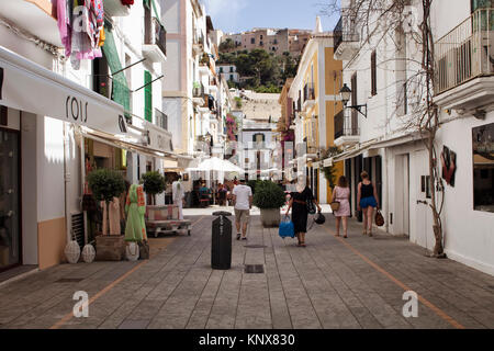 View of people walking on one of narrow, historical shopping streets in Ibiza old town. Image reflects culture and lifestyle of the island. Stock Photo