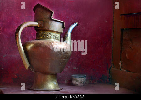 Ancient copper jug handmade on a background of maroon wall. Stock Photo
