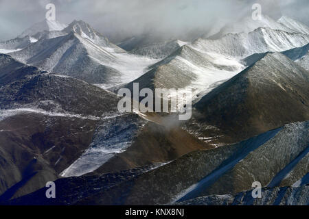 Mountain valley, brown gorges, slopes and peaks are covered with snow, gray winter sky. Stock Photo