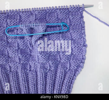 Basket weave pattern knitted on knitting needle in lilac color wool.   Stitch holder in place marking off extra stitches to be knit later Stock Photo