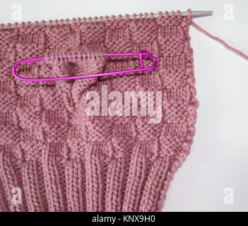 Basket weave pattern knitted on knitting needle in rose color wool.   Stitch holder in place marking off extra stitches to be knit later Stock Photo