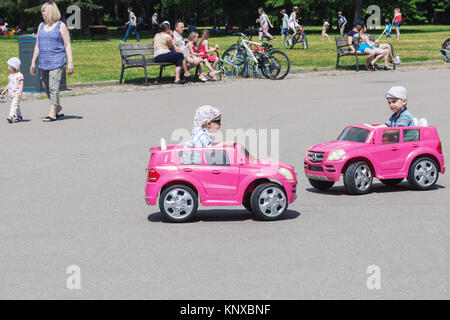 Two little boys driving toy electric cars in a park at sunny summer day in Vilnius, Lithuania Stock Photo