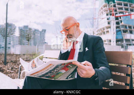 middle age man contemporary businessman business call reading newspaper sitting bench - remote working, news, business concept Stock Photo