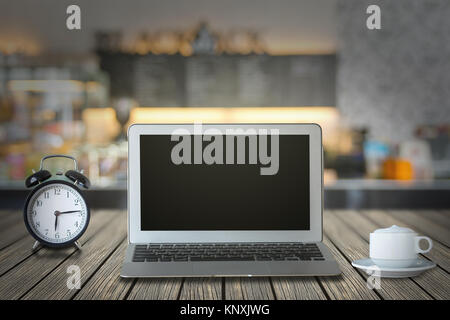 Laptop with retro alarm clock and coffee cup on the wood table over the coffee shop blurred background Stock Photo