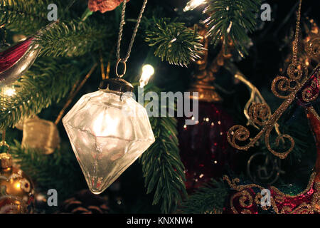 Mercury Glass diamond shaped ornament hangs from a branch on an old fashioned vintage Christmas tree with other ornaments in the backgound Stock Photo