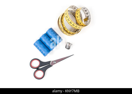 Sewing supplies and tools, three blue sewing threads, yellow measuring tape with black numbers, small closed scissors and metal thimble Stock Photo