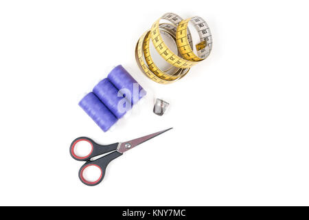 Sewing supplies and tools, three medium purple sewing threads, yellow measuring tape with black numbers, small closed scissors and metal thimble Stock Photo