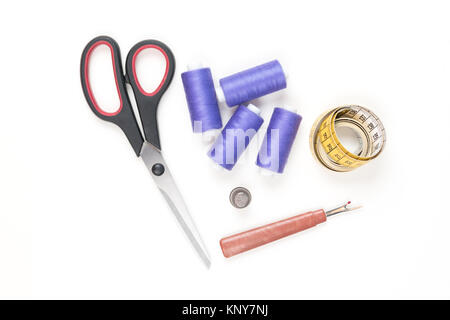 Sewing supplies and tools, medium purple sewing threads, yellow measuring tape with black numbers, big scissors, metal thimble and seam ripper Stock Photo