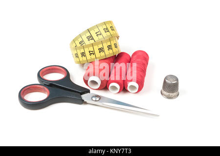 Sewing accessories and tools. Red sewing threads, black scissors, yellow measuring tape and thimble on a white background. Stock Photo
