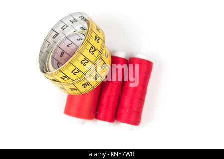 Sewing supplies, red thread on white coil and yellow measuring tape with black numbers on a white background. Tailoring supplies. Stock Photo