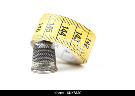 Metal silver sewing thimble with yellow measuring tape on a white background. Sewing accessories and tools Stock Photo