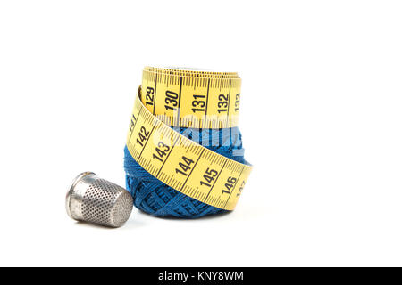 Yellow measuring tape on top of blue sewing thread with silver thimble on a white background Stock Photo