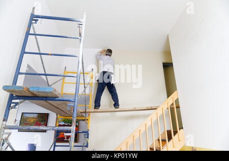 A decorator painting a house interior, difficult access involving scaffolding Stock Photo