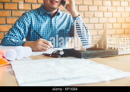 Architect or engineer talking on smart phone working in office on blueprint. Architects workplace Stock Photo