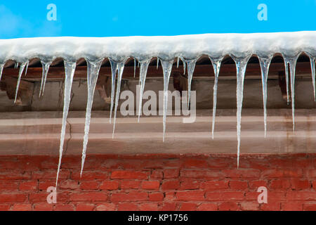 White snow on the roof of a red brick house and icicles hanging from a slate roof. Stock Photo