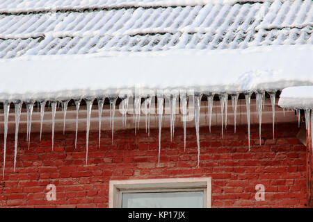 White snow on the roof of a red brick house and icicles hanging from a slate roof. Stock Photo