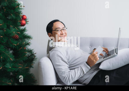 Senior asian man shopping using latop and credit card by the christmas tree Stock Photo