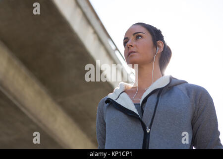 Thoughtful female jogger listening to music on a sunny day