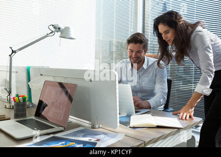 Male and female executives discussing over laptop in office Stock Photo