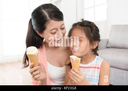 smiling beautiful mother looking at pretty little daughter eating ice cream feeling happiness and enjoying summer season at home together. Stock Photo
