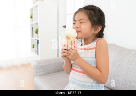 beautiful attractive little girl children eating ice cream dessert at home and showing enjoying expression in summer season. Stock Photo