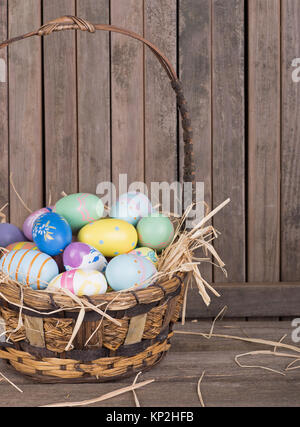 Colorful Easter eggs in a basket on a wooden surface Stock Photo