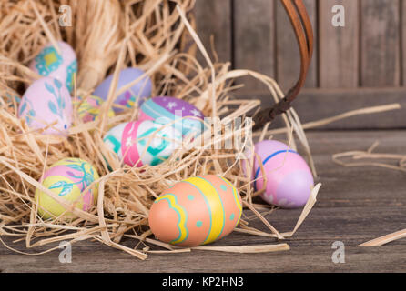 Colorful Easter eggs spilled from a basket on a wooden surface Stock Photo