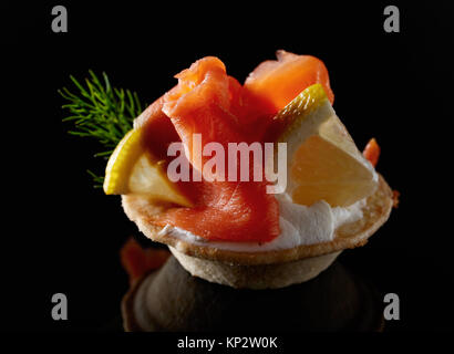 Tartlets with salmon , cream and a slice of lemon on a black background. Stock Photo