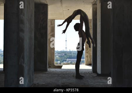 Silhouette of couple of ballet dancers who posing on the concrete floor of the unfinished building on the cityscape background. Guy holds a girl in th Stock Photo